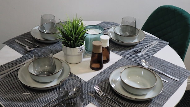 A round dining table set with plates, bowls, cutlery, glasses, and a potted plant.