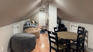 Un espacio tipo loft con comedor, un sofá gris, una pared de ladrillo blanco y piso de madera.
