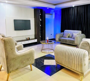 Relax in this stylish living space, featuring a flat-screen TV, a tufted sofa, and a round coffee table.