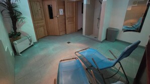 Une pièce avec une grande plante en pot, des portes en bois, un espace douche et une chaise bleue.
