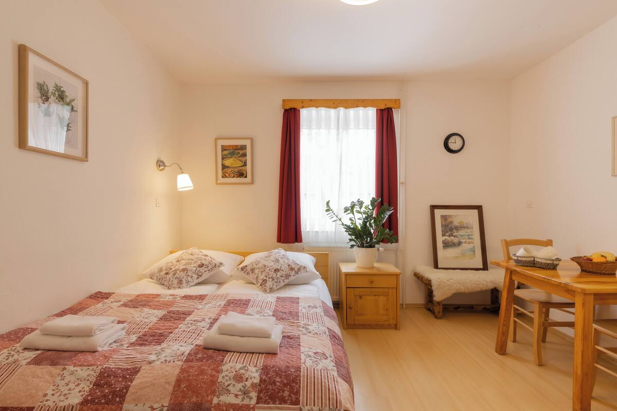 A neatly arranged bedroom with a bed, bedside table, chair, and a small dining table.