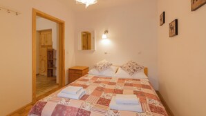 Une chambre avec une porte en bois, une table de chevet, un lit avec une couette et un luminaire fixé au mur.