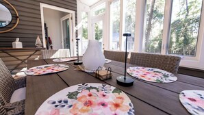Comedor luminoso con una mesa de madera, sillas de mimbre y vistas a árboles a través de amplios ventanales.