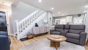Una sala moderna con un sofá gris, una mesa de centro de madera y una escalera con barandillas blancas.