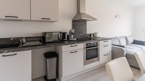 Een moderne keuken met een magnetron, broodrooster en oven, een prullenbak, en een grijze bank in de woonkamer.