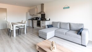 Een moderne woonkamer met een grijze bank, een houten salontafel, en een eethoek met een witte tafel en stoelen.