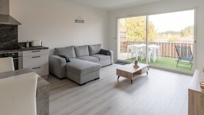 Een moderne woonkamer met een grijze bank, een houten salontafel en een keuken met een fornuis en kastjes.