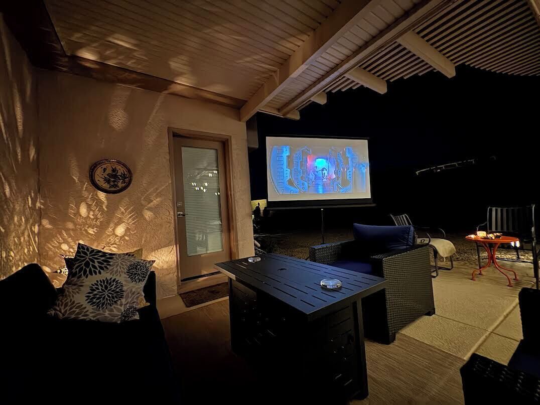 Eine Terrasse im Freien mit Fernseher, Korbmöbeln und einem Tisch.