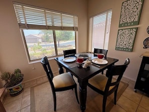 Un coin repas avec une table dressée pour quatre personnes, des chaises, une plante en pot et des œuvres d’art accrochées aux murs.