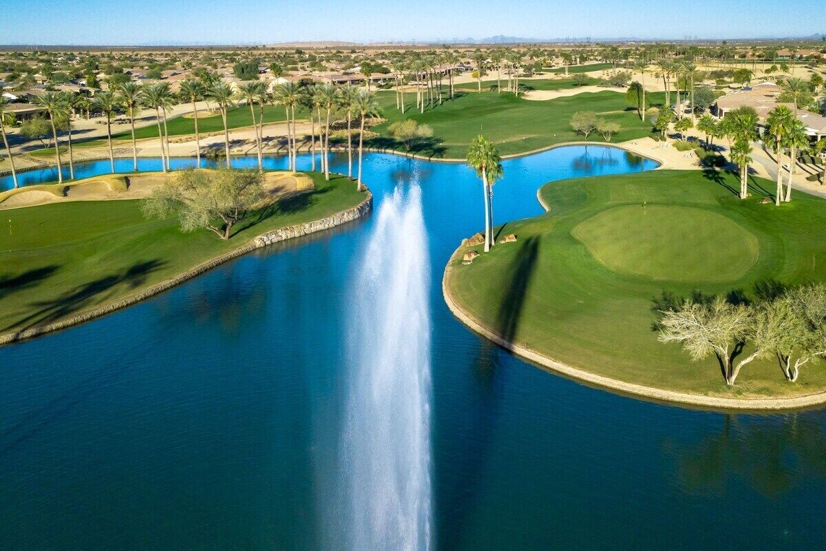 A golf course with a water feature, palm trees, and a clear sky.