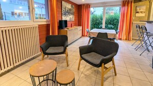 Een gezellige kamer met een eethoek, twee fauteuils, een kleine tafel en een televisie op een houten kast.