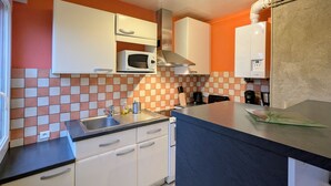 Een kleine keuken met witte kastjes, een magnetron, een gasfornuis en een spoelbak.