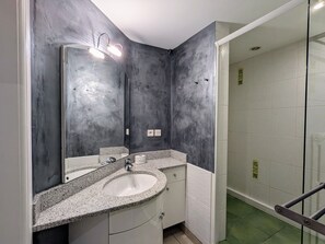 Une salle de bain moderne avec un lavabo sur un plan de travail en granit, un grand miroir et une douche à l’italienne dotée d’une porte en verre.