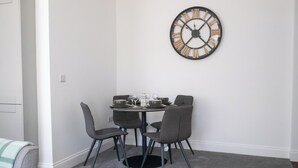 A dining area with a round table, four chairs, and a large wall clock.
