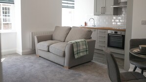 A modern kitchen with a grey sofa, a dining table, and a window with blinds.