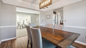 Een eetkamer met een houten tafel en stoelen, een kroonluchter en een uitzicht op een andere kamer.
