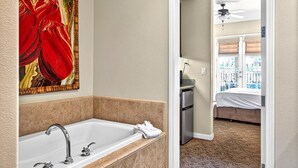 A bathroom with a bathtub, a large mirror, and a painting of a red flower.