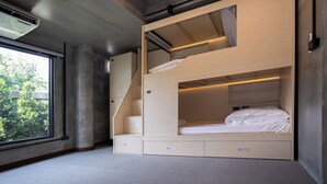 Une chambre avec un lit superposé, une fenêtre, un bureau intégré et des tiroirs de rangement.