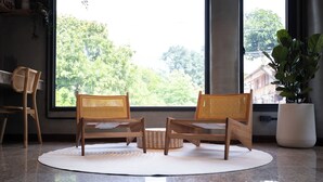 Une pièce avec une grande fenêtre, deux fauteuils en osier, une petite table ronde et une plante en pot.
