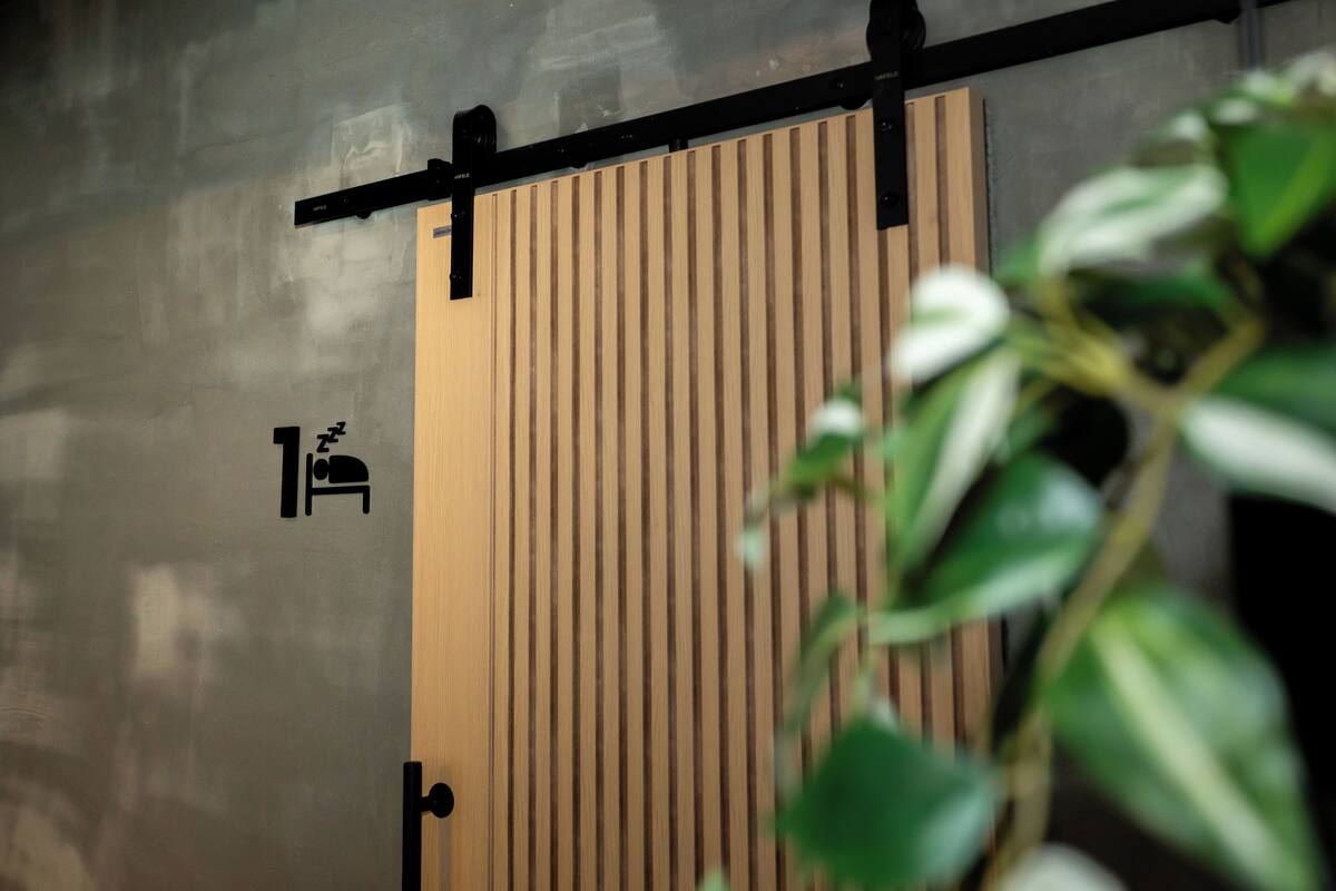 A wooden door with vertical slats, a black horizontal bar, and a small icon indicating a room with a bed.