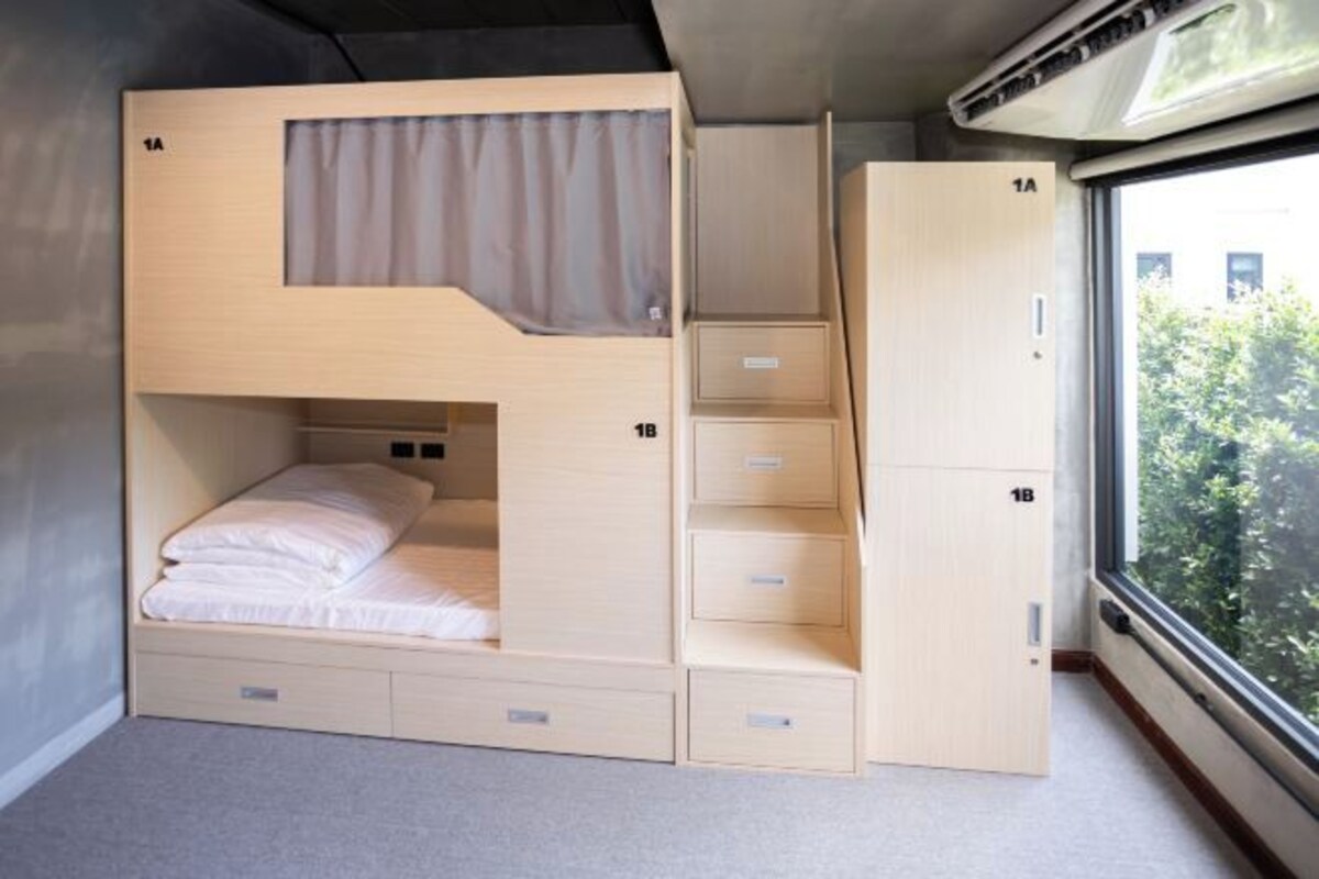 Une chambre compacte, de type cabine, avec un lit, des rangements intégrés et une fenêtre donnant sur un espace verdoyant.