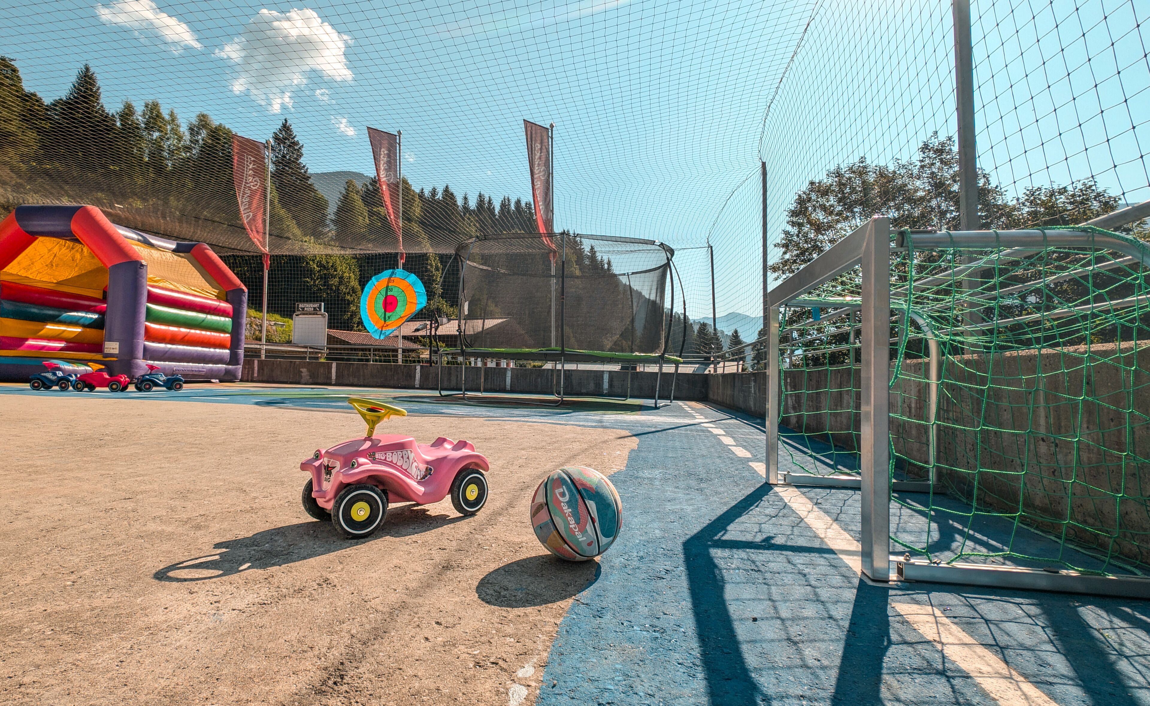 Zona de juegos infantiles con un arco de fútbol, estructuras inflables y un pequeño coche de juguete rosa.