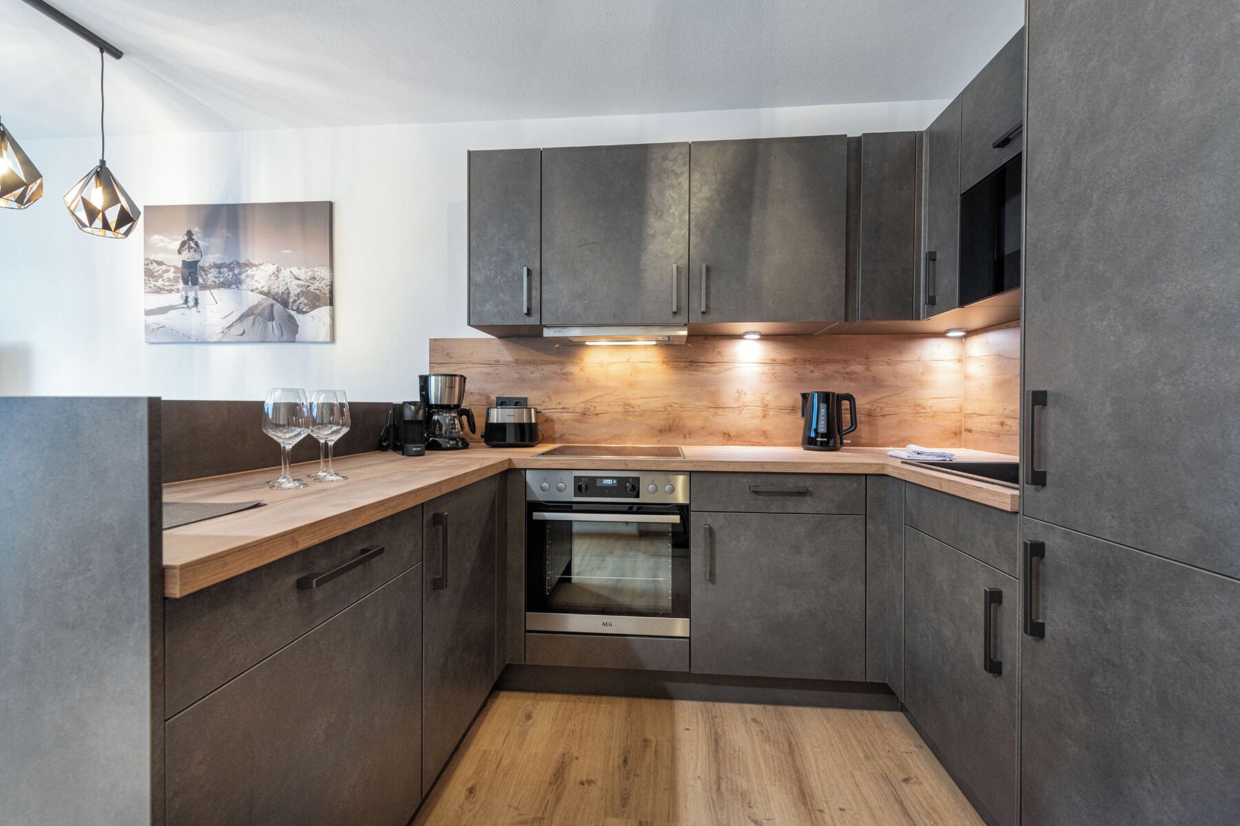 A modern kitchen with dark cabinets, a wooden countertop, a built-in oven, and a coffee maker.