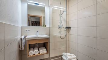 A modern bathroom with a glass-enclosed shower, a sink with a mirror above it, and a shelf with towels.