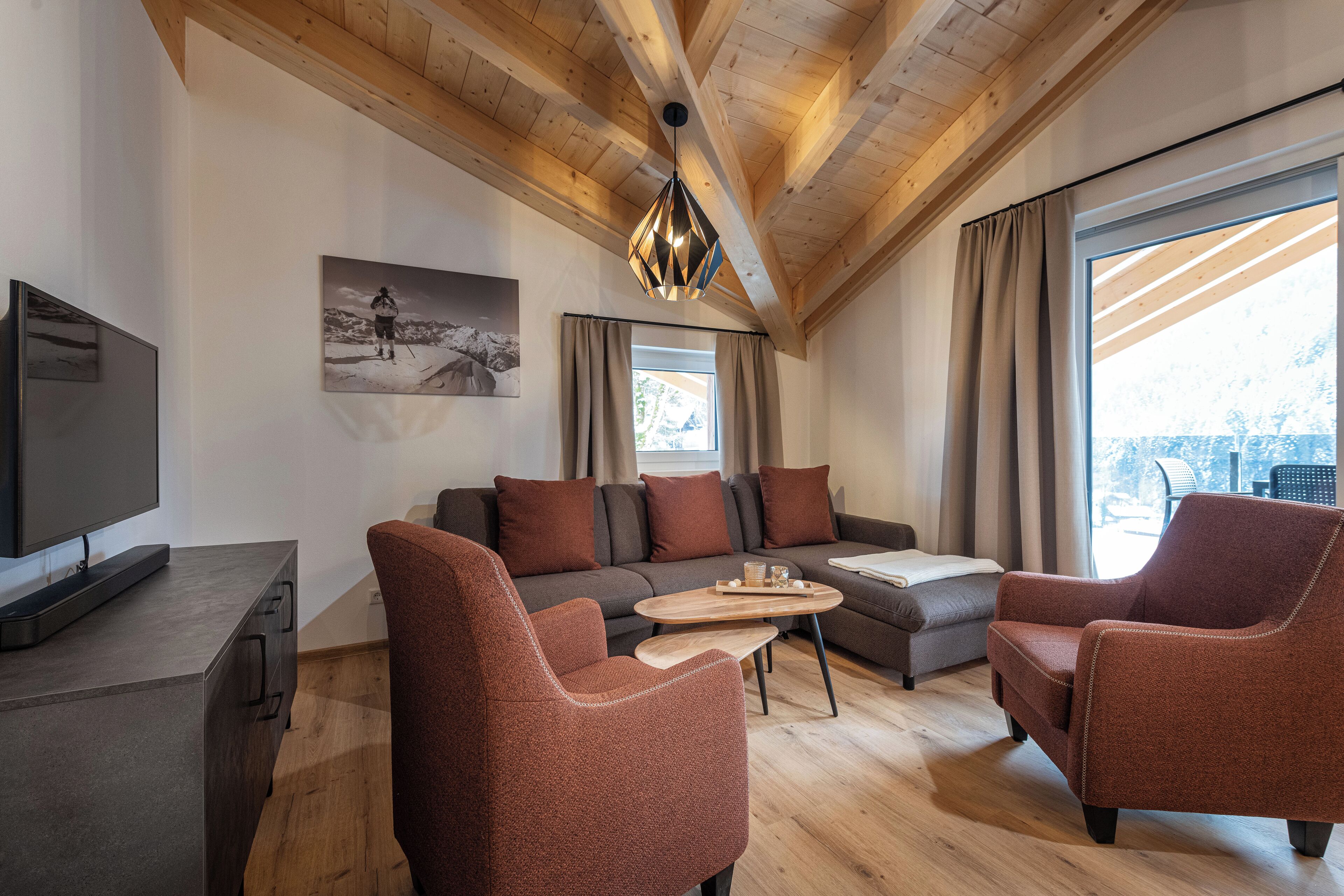 A modern living room with a wooden ceiling, a flat-screen TV, a sofa, two armchairs, a coffee table, and a painting on the wall.