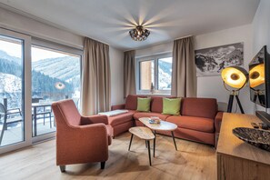 A modern living room with a sofa, armchair, and coffee table, large windows with a mountain view, and a ceiling light fixture. - AlpenParks Residence Glemmrise Viehhofen (Viehhofen)