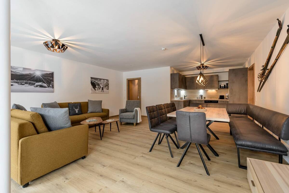 Ein modernes Wohnzimmer mit einer Couch, Sesseln, einem Esstisch und einer Küche im Hintergrund.