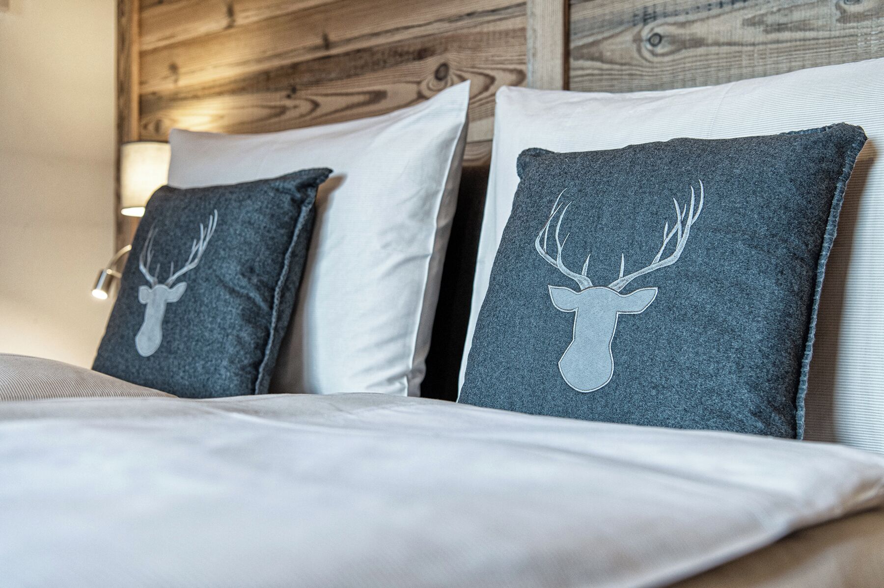 A bed with two pillows, one with a deer head design and the other plain.