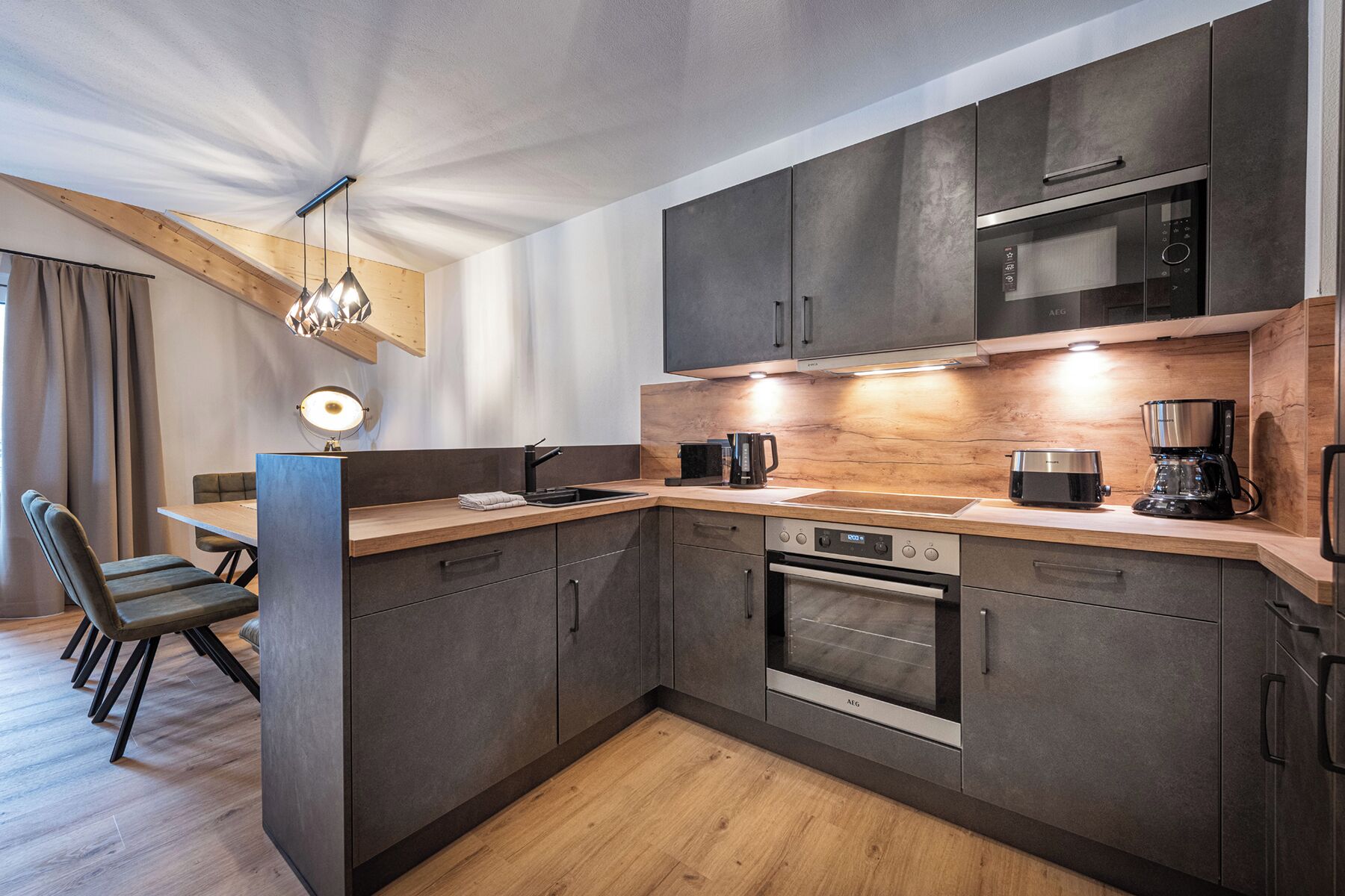 Una cocina moderna con armarios oscuros, encimera de madera y electrodomésticos integrados, incluyendo un microondas y un horno.