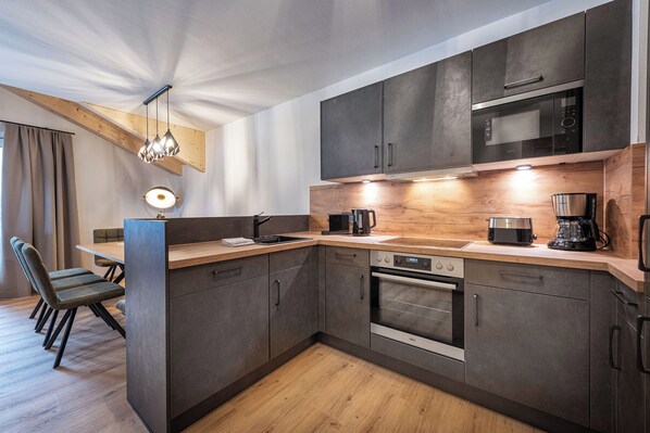 A modern kitchen with dark cabinetry, a wooden countertop, and built-in appliances including a microwave and oven. - AlpenParks Residence Glemmrise Viehhofen (Viehhofen)