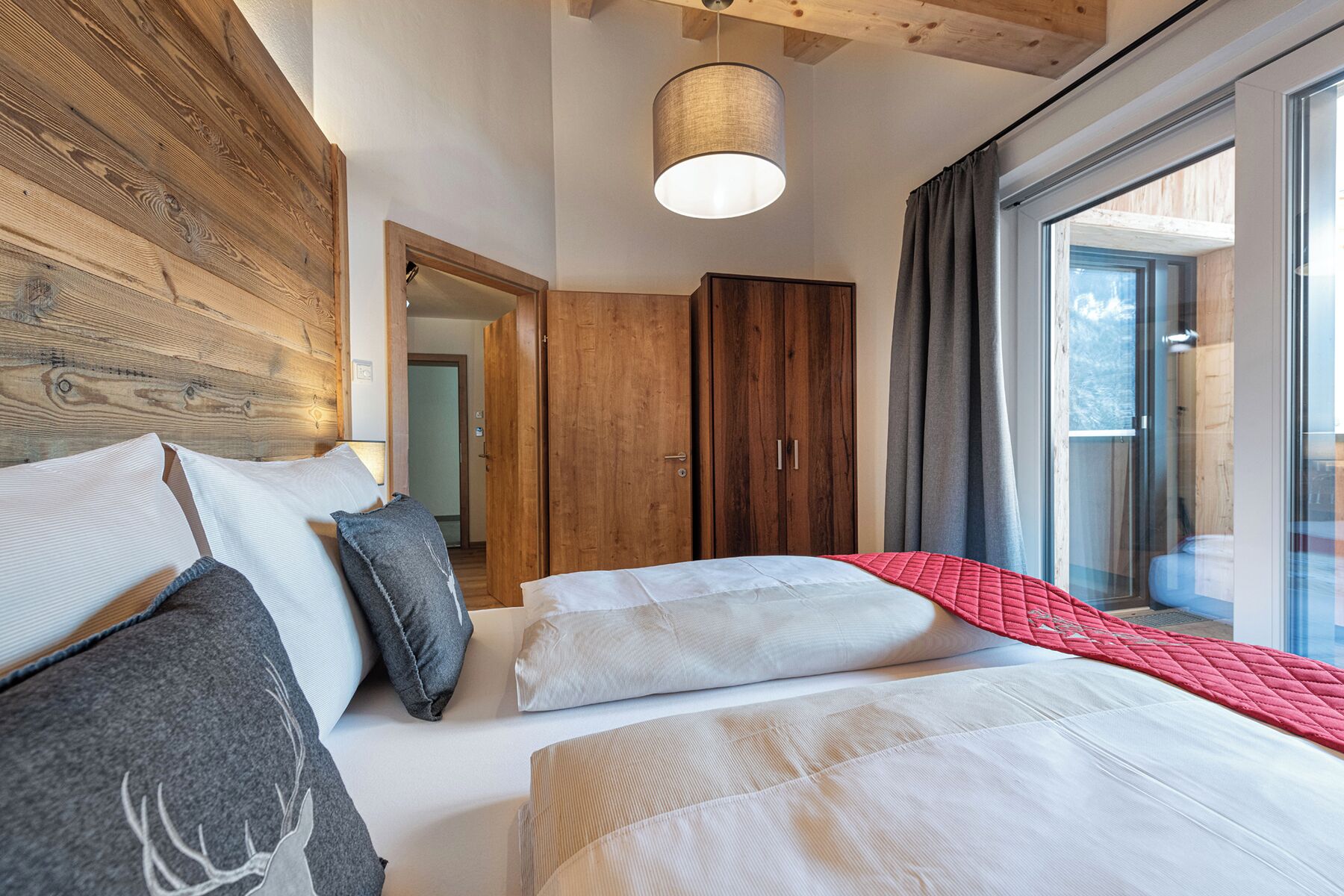 A bedroom with a large bed, a wooden headboard, a wardrobe, and a window with curtains.