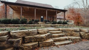 A wooden cabin with a covered porch, stone steps, and a stone wall.