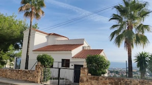 A two-story house with a tiled roof, surrounded by stone walls and palm trees. - Villa with stunning sea view, private pool and garden (Alcocéber)