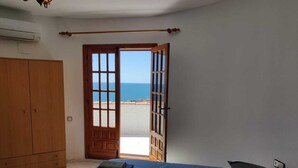 A bedroom with a large bed, a wooden wardrobe, and a view of the sea through an open door. - Villa with stunning sea view, private pool and garden (Alcocéber)