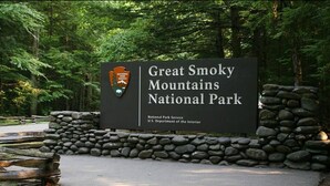 Placa para o Parque Nacional Great Smoky Mountains, com um muro de pedra e uma cerca de madeira ao fundo.
