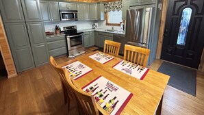 Cozinha com armários cinza, eletrodomésticos em aço inoxidável e mesa de jantar de madeira com jogos americanos.