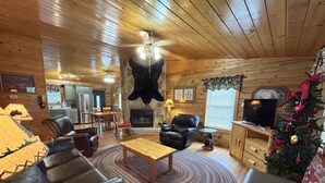 Interior acolhedor de uma cabana com lareira, móveis de couro, área de refeições e uma árvore de Natal.