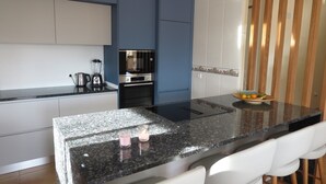 A modern kitchen with a black granite countertop, a built-in stove, and a microwave. There are white chairs and a fruit bowl on the counter. - beautiful villa with sea and mountain views. (El Campello)