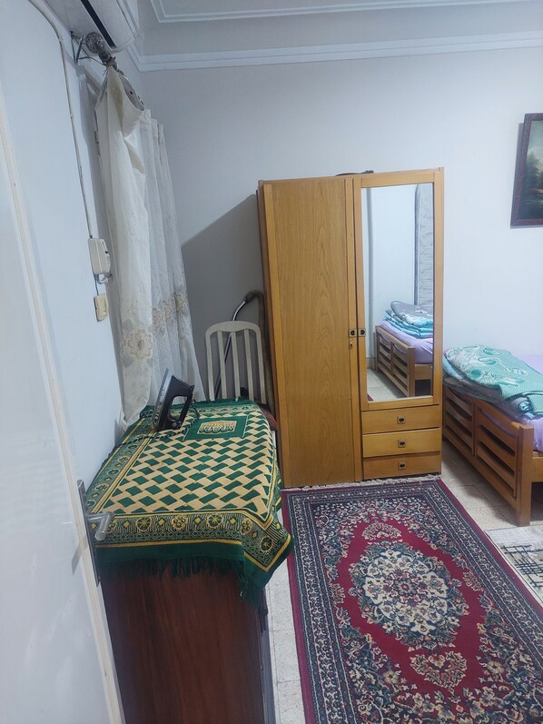 A bedroom with a wooden wardrobe, a bed with a patterned bedspread, a small bedside table, and a decorative rug.
