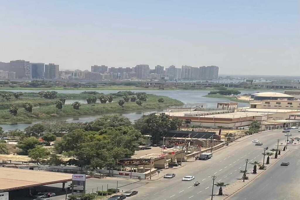 A cityscape with a river, buildings, and a road with vehicles.