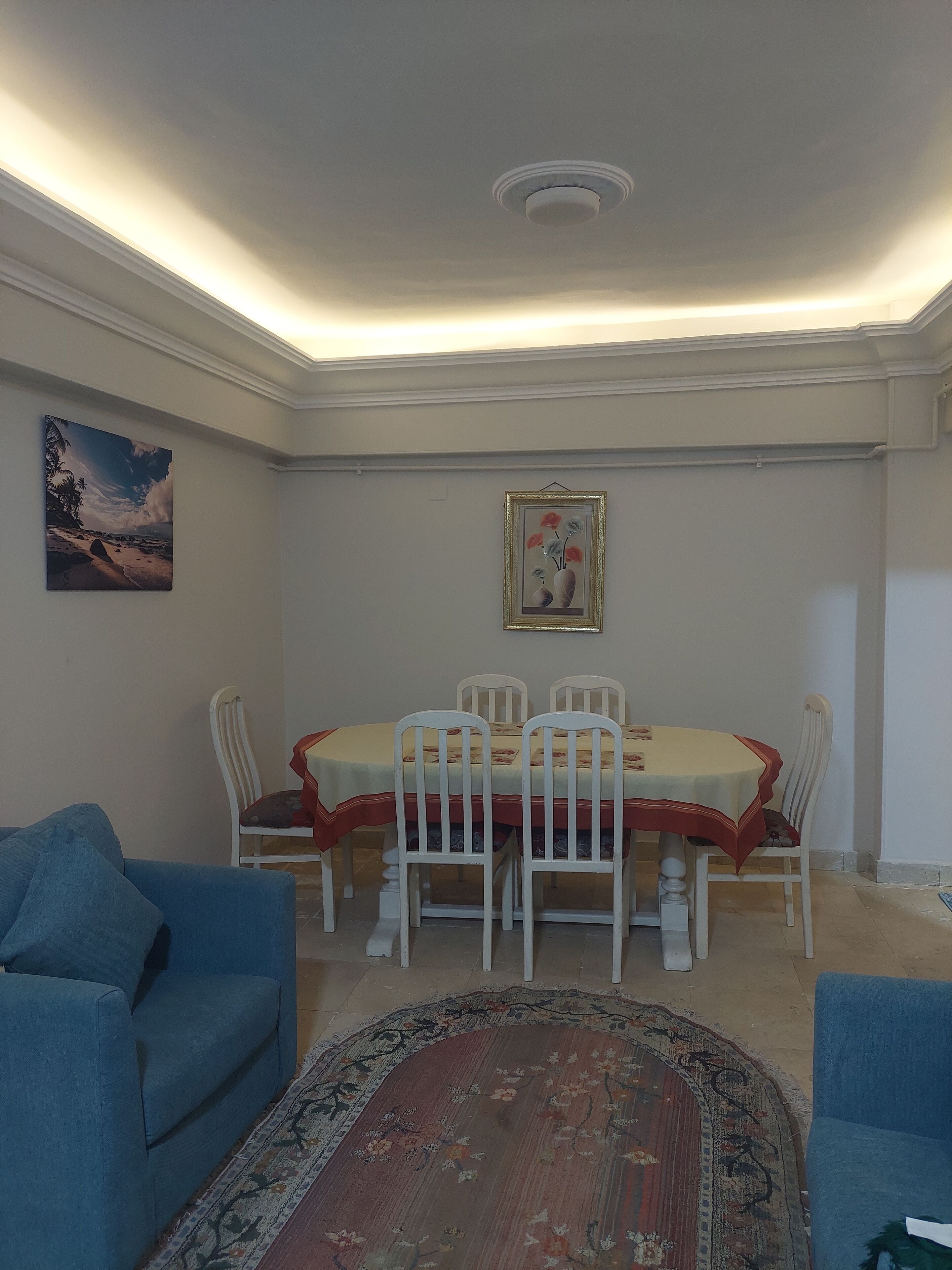 A dining area with a table and chairs, a painting on the wall, and a blue sofa.