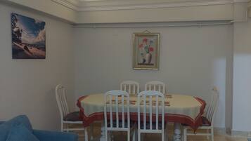 A dining area with a table and chairs, a painting on the wall, and a blue sofa.