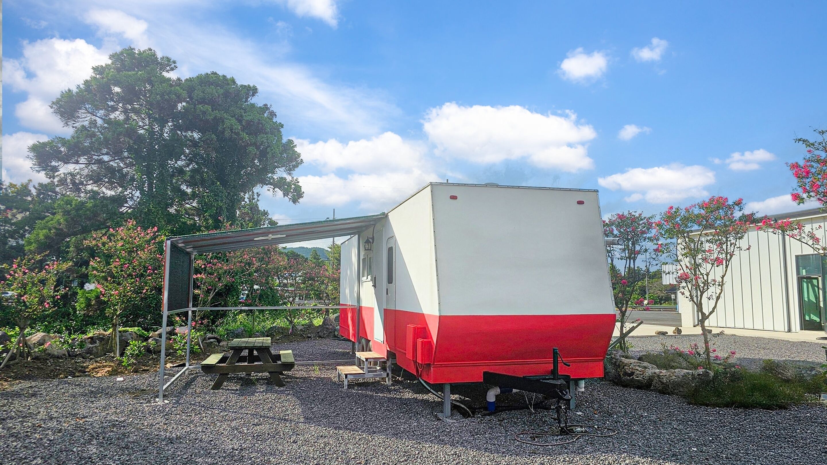 A stationary vehicle with a red and white color scheme, parked on a gravel surface with a picnic table nearby.