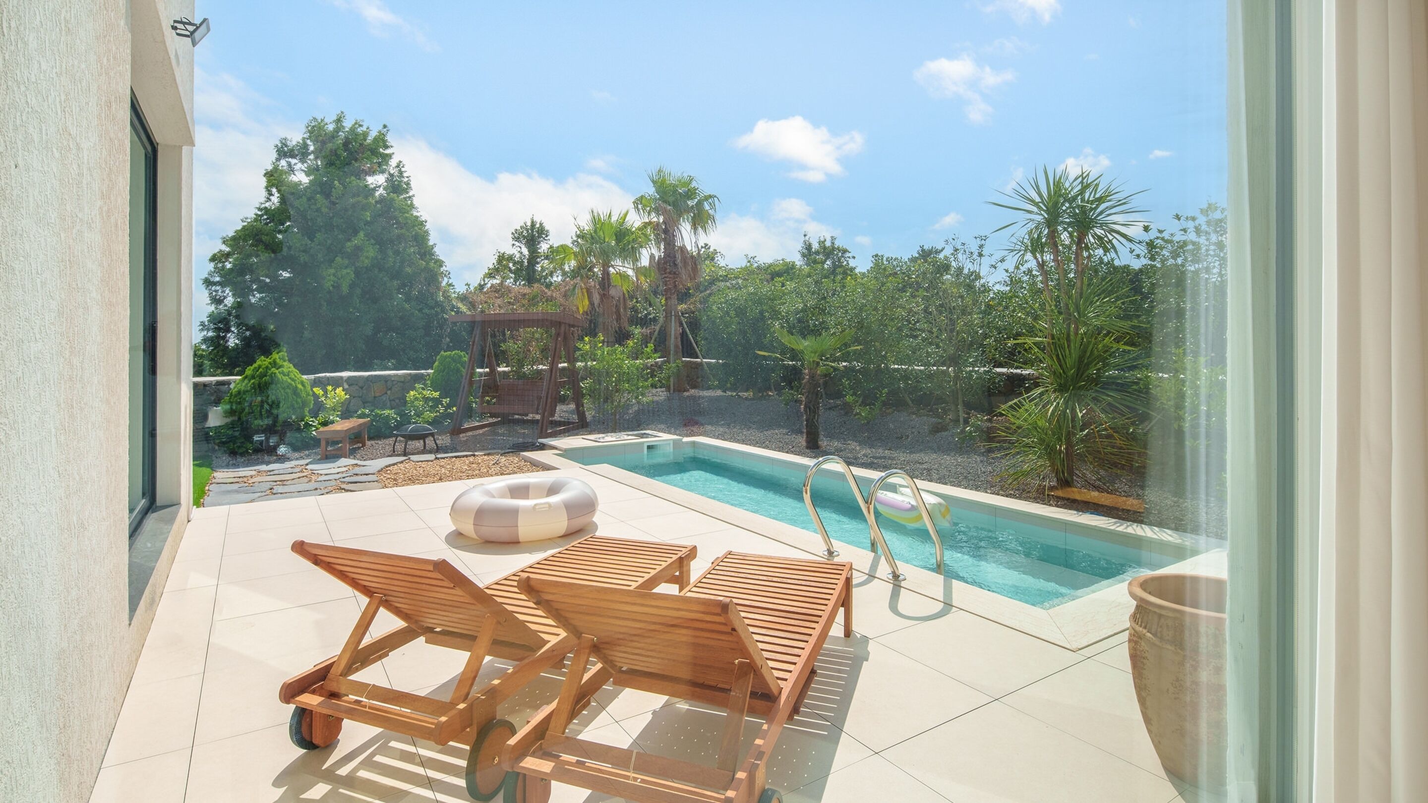 Un espace aménagé au bord de la piscine, comprenant deux chaises longues en bois, une petite table et une balançoire.
