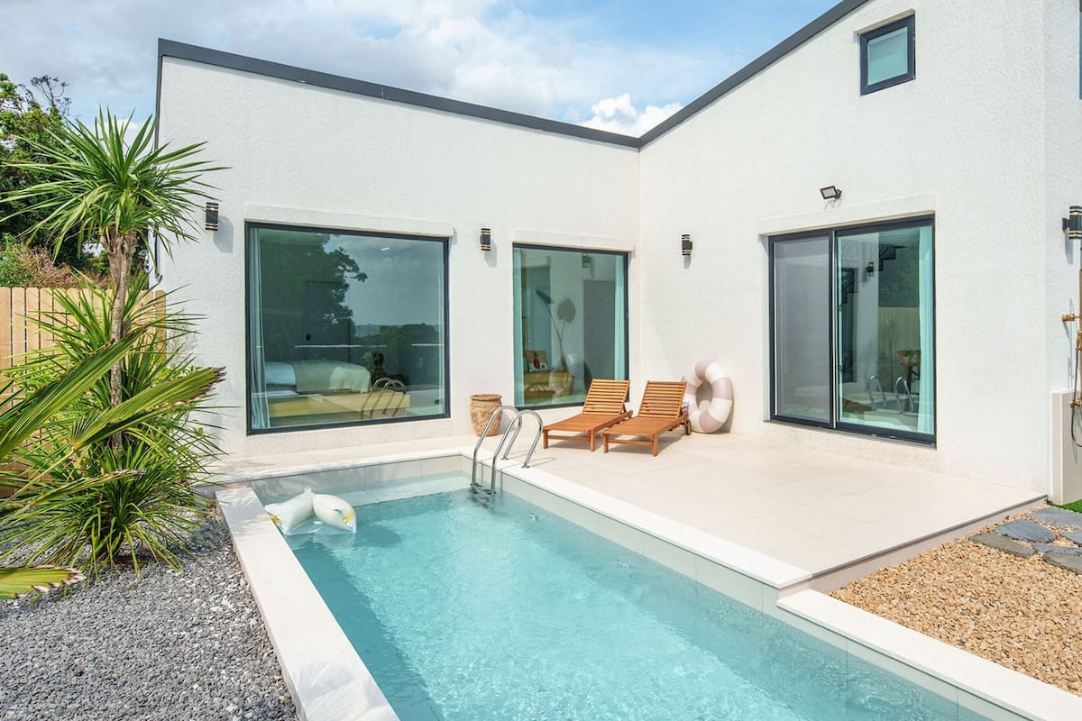 Ein modernes Haus mit Swimmingpool, großen Fenstern und einer Terrasse mit Liegestühlen.