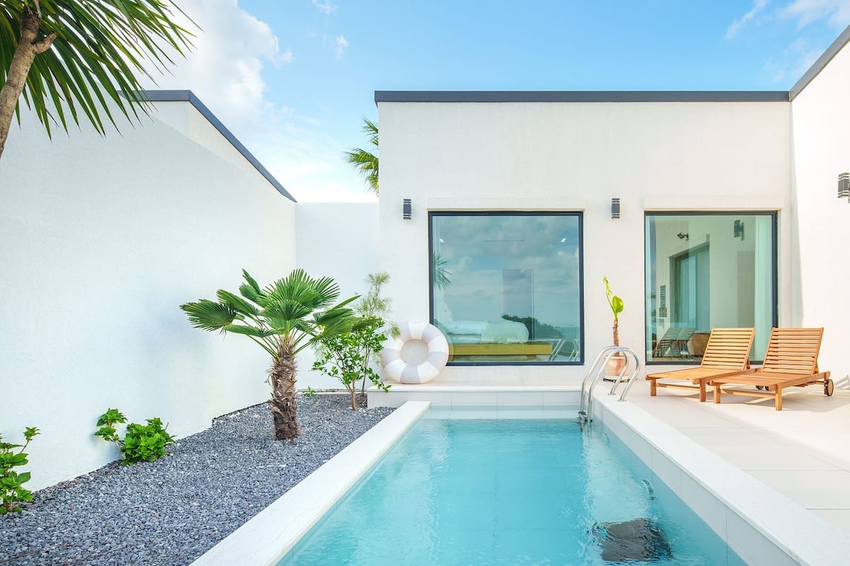 Ein moderner Poolbereich mit freiem Blick auf den Pool, eine Holzterrasse mit Liegestühlen und eine große Schiebeglastür, die zu einer überdachten Terrasse führt.